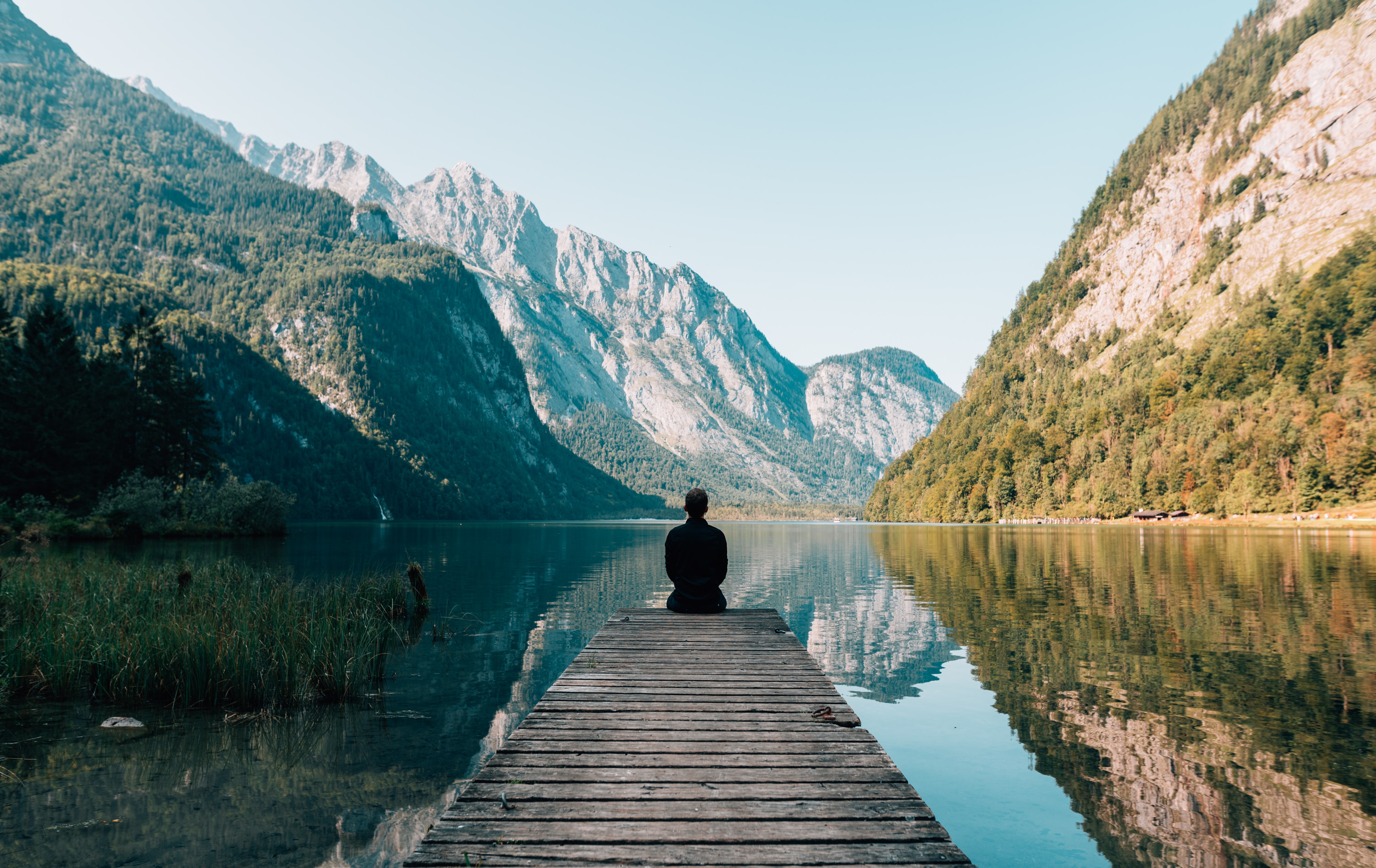 Photo of a person sitting on a pier looking at a river and mountains